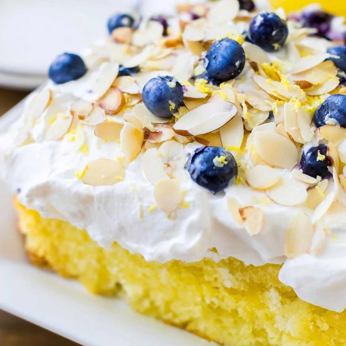 Moist lemon blueberry poke cake topped with fluffy whipped cream and crunchy toasted almonds