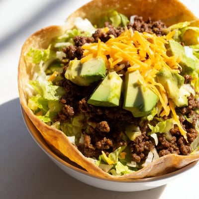 Ground beef taco salad in a homemade baked tortilla bowl with black beans, corn, and cheddar cheese.
