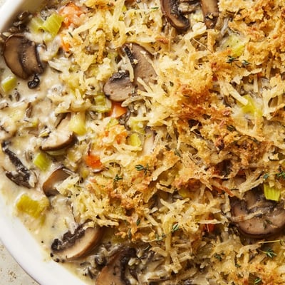 Golden-brown Creamy Mushroom and Wild Rice Casserole with Thyme is spooned onto a rustic plate, served as a cozy vegetarian main dish.
