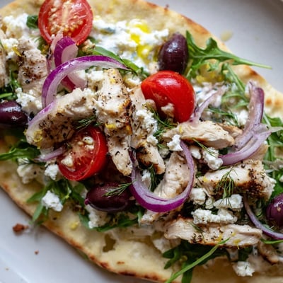Freshly baked Zesty Lemon Herb Chicken Flatbread drizzled with olive oil and scattered with arugula and olives.