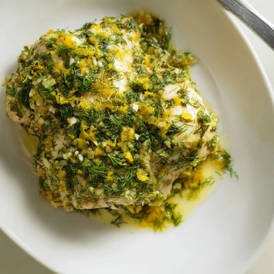 Tender paleo lemon dill chicken fresh from the oven, garnished with lemon slices and chopped dill on a platter.