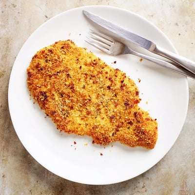 A close-up view of cooked Air Fryer Breaded Chicken Breast highlights the crunchy panko crust and golden Parmesan breading on a white ceramic plate.