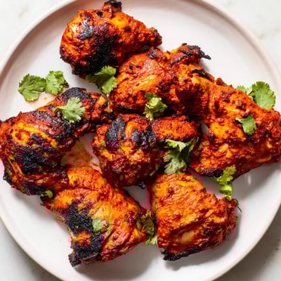 Juicy Tandoori Chicken drumsticks roasted in the oven with vibrant spices, next to lemon wedges and basmati rice on the table.