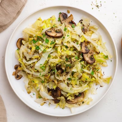 Steaming Vegetarian Cabbage Mushroom Sauté served in a white bowl, garnished with fresh parsley and a lemon wedge on the side.