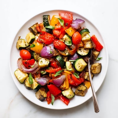 A sheet pan of tender classic Mediterranean roasted vegetables alongside cherry tomatoes and red onion wedges